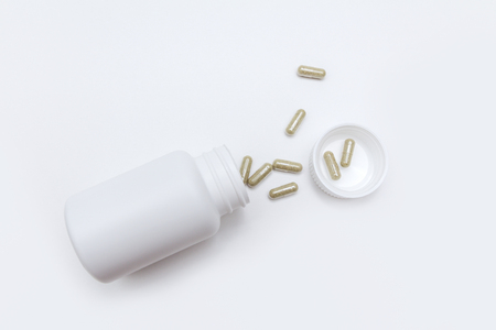 green capsules with vitamins from a white open bottle on a white backgroundの写真素材
