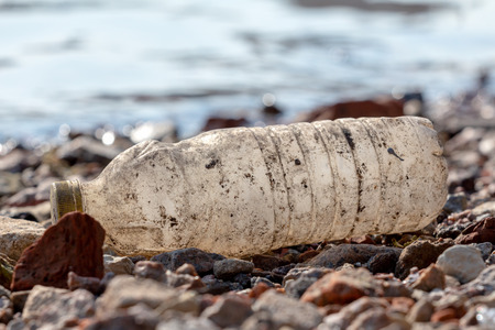 discarded dirty plastic bottle with a yellow cap on the shore near the water. plastic pollutionの写真素材