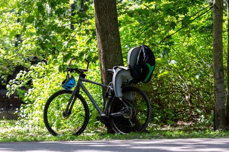 Bicycle with a child seat and a backpack over the rear wheel in a park near a green tree. Active holiday with a child on a sunny summer sunny day in a green parkの写真素材