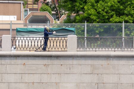 a worker in a gas mask cleans the fence and wall of the quay from rust and old paint with compressed air. repair and painting of the embankment fenceの写真素材
