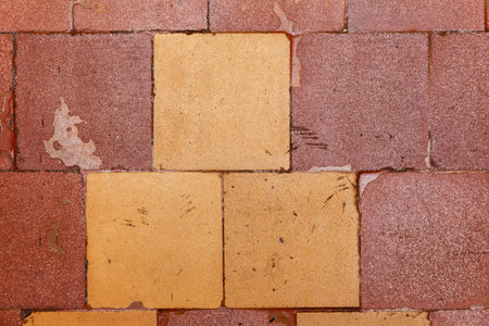 Old square tiles on the floor with cracks and scuffs. yellow and brown