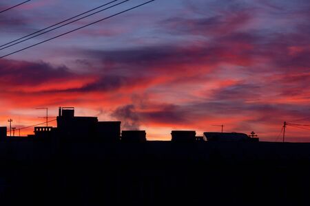 dark silhouettes of city roofs on the background of colorful magnificent dawn with bright red-pink cloudsの写真素材