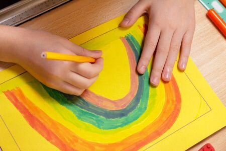 Hands of a child painting a rainbow on a sheet of paper at a deskの写真素材