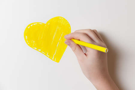 Girl draws a felt-tip pen a yellow heart on the wall of the room. Health and happy childhood concept.の写真素材