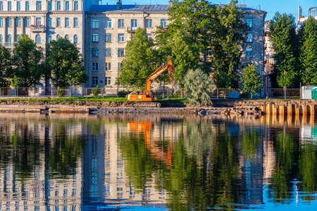 St. Petersburg, Russia - August 19, 2020: Reconstruction and strengthening of the Martynov embankment on the bank of the Srednyaya Nevka. The excavator is reflected in the riverのeditorial素材