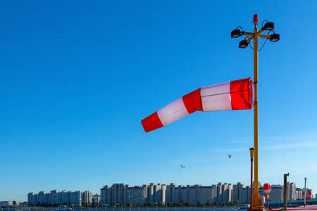 Windsock against a blue sky with birds and city buildings in the backgroundの写真素材