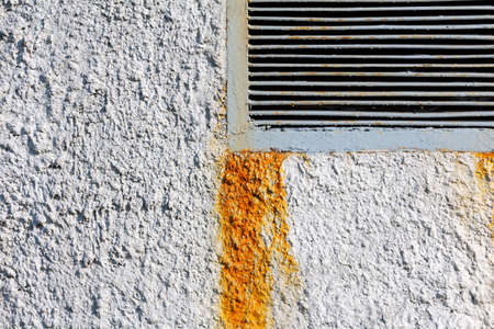 Edge of a rectangular ventilation grill in a roughly plastered concrete wall with rust stains. Industrial backgroundの写真素材