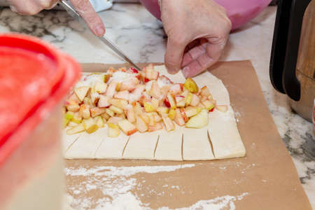 Woman making apple pie on parchment paper on marble kitchen tableの写真素材