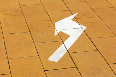 A white curved arrow is drawn on the yellow paving slabs. Direction of pedestrian trafficの写真素材