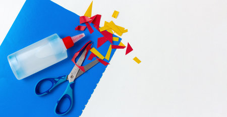 Scraps of cut colored paper with scissors and glue on the children's tableの写真素材