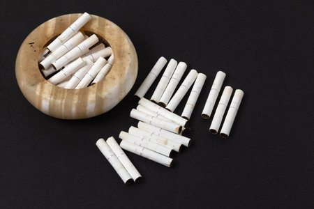 Close-up photo of a pile of cigarette butts of tobacco heating technology in an ashtray and scattered on the table on a dark backgroundの写真素材