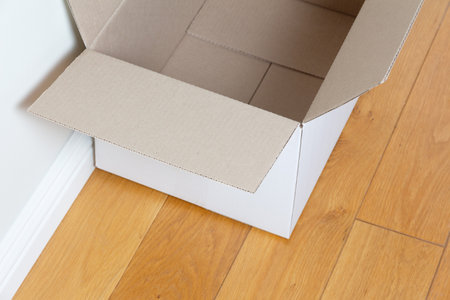 Empty open cardboard box on the wooden floor of the roomの写真素材