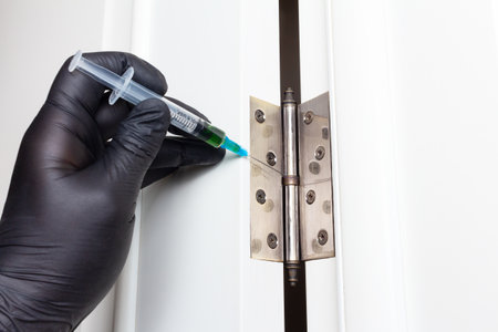 A man's hand with a syringe filled with machine oil lubricates the door hinges. Adjustment and elimination of door hinge creaksの写真素材