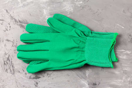 Two green work gloves with a protective layer on the palms and fingers on a gray cement background. Personal protective equipment against mechanical damageの写真素材