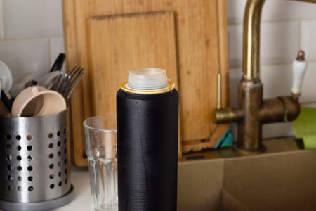 Old water filter cartridge in the kitchen on the background of sinks and dishes