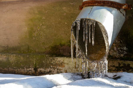 Icicles on the downspout of the building facade. Melting ice and snow in spring. Close-up drainpipe with long transparent iciclesの写真素材