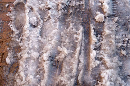 Melted snow and snow slurry on the sidewalk with footprints and bicycle tire printsの写真素材