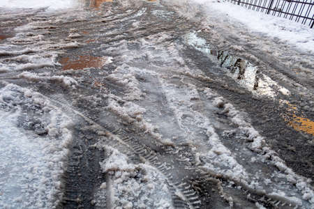 Melting wet snow and slush with puddles on the road with tire marks. Thaw with morning frostsの写真素材