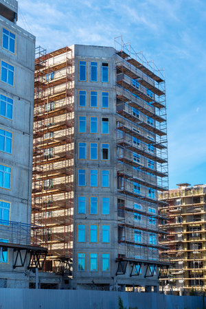Construction site of new comfortable high-rise residential buildings with scaffolding against a blue...