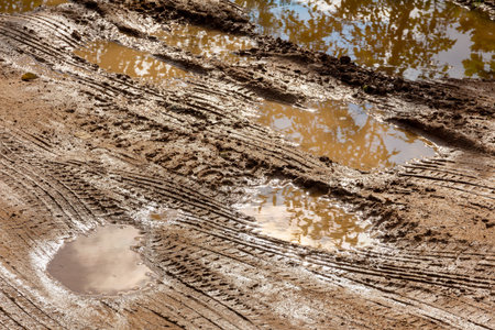 Dirty wet sandy road with puddles and car tire marks