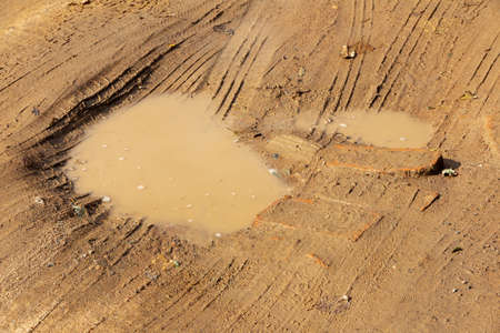 Dirty wet sandy road with puddles and car tire marksの写真素材