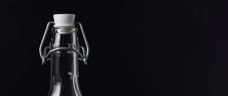 Transparent glass bottle closed with vintage wire stopper on black background with space for text on the right sideの写真素材