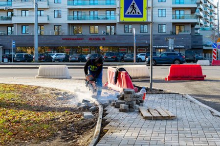 Saint-Petersburg, Russia - October 24, 2022: A worker cuts paving slabs with a petrol circular saw on a city street. A man without a hardhat and goggles works with a saw on the sidewalkのeditorial素材