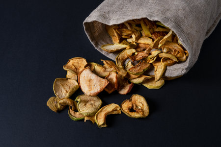 Dried apple slices in an eco-friendly canvas bag lie on a dark surfaceの写真素材