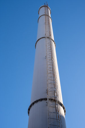 Tall metal chimney with ladder against blue skyの写真素材