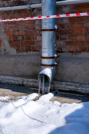 Downpipe with icicles and snow closed barrier tape signal line prohibits passageの写真素材