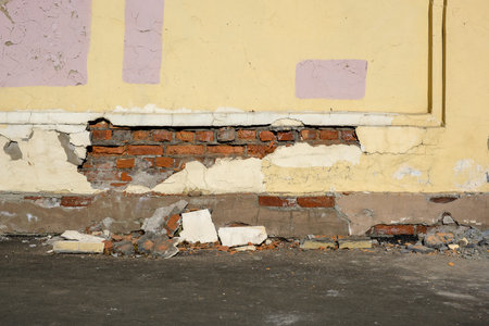 Old brick wall with plaster falling off the sidewalkの写真素材