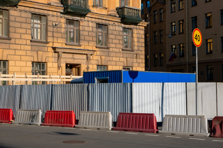 Fenced territory of a construction site with a fence and plastic barriers on a city street against the background of old housesの写真素材