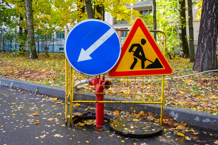 Road signs and a red fire hydrant with a hose in an open fenced manhole. Pumping water and eliminating the accidentの写真素材