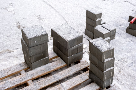 Stacks of new paving slabs on a wooden pallet under the snow after the first snowfall. Construction in winterの写真素材