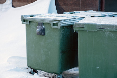 Green plastic dumpster or waste and garbage containers in snow on a winter streetの写真素材