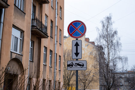 Combination of international road signs "No Parking" or "No Stopping" and "Vehicle Evacuation" against the backdrop of city buildingsの写真素材