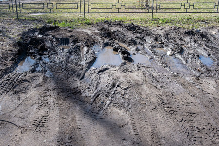 Fenced dirt parking for cars with tire marks, puddles and mud