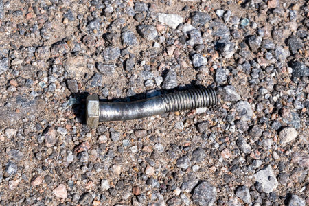 Damaged crooked bolt on a crushed stone roadの写真素材