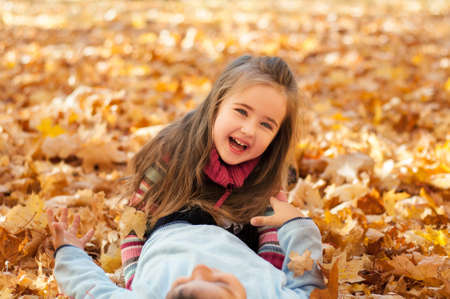 Happy children in autumn park lying on yellow maple leaves, little girl lies on a boy and laughingの写真素材