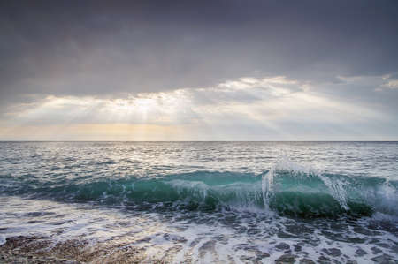Sea wave, and the sun's rays pass through the cloudsの写真素材