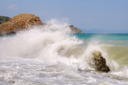 Big sea wave breaking on the shore and left behind huge parts of foam and sprayの写真素材