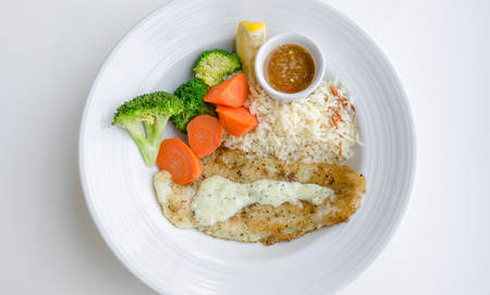 grilled dory, juice, accompanied by garlic herb rice and veggies with spicy seafood dip, on white dish.の写真素材