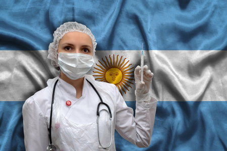 Young woman doctor in medical uniform on the background of the national flag of Argentina is holding a syringe. The concept of a new vaccine against the disease, flu vaccine vaccinationの写真素材
