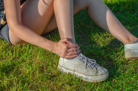 Young woman athlete outdoors sitting on grass touching painful twisted ankle. Training athlete runnerの写真素材