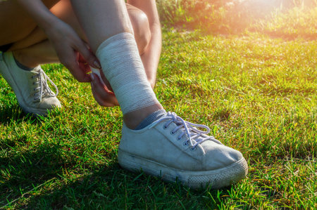 Young woman runner bandages her legs to protect tendons during long run and physical activity. Evening workout outdoors in the park.の写真素材