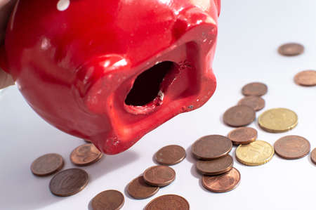 The process of shaking money out of your red piggy bank. Euro coins fell from the hole in the piggy bank onto the table. The concept of finding money, crisis, poverty.の写真素材