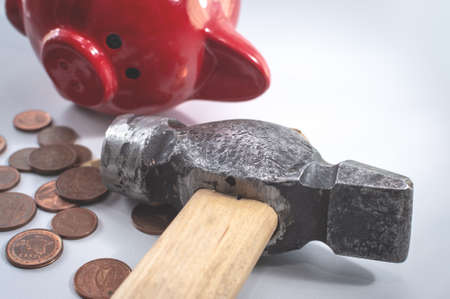 A hammer and a broken red piggy bank, next to a pile of small euro coins. The concept of finding money, shopping, crisis, poverty, payment.の写真素材