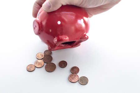 A man's hand holds a piggy bank and shakes out coins from it. The process of shaking money. Euro coins fall on the table from the hole in the piggy bankの写真素材
