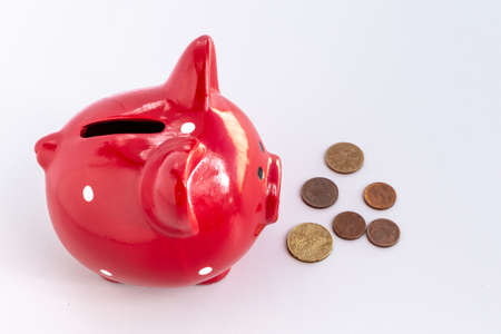 A red piggy bank with a small stack of euro coins in front of it. Thinking smart piggy bank. Concept of investing money, managing money and saving money. Side viewの写真素材