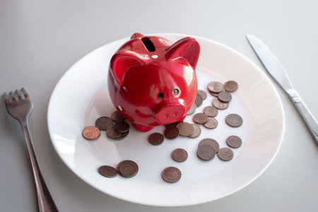 Side view of a red piggy bank on a plate with cutlery. Eat savings, consumer savings concept, eating...